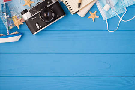 Overhead photo of camera ship starfish map organizer pen mask and antiseptic isolated on the blue wooden background with copyspaceの写真素材