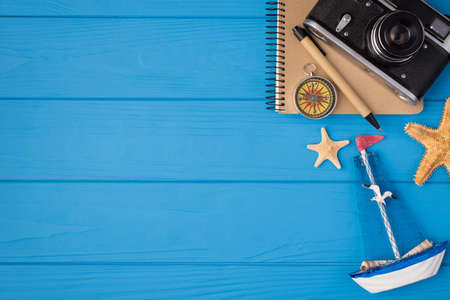 Overhead photo of shop camera compass starfish notebook and pen isolated on the blue wooden background with empty spaceの写真素材