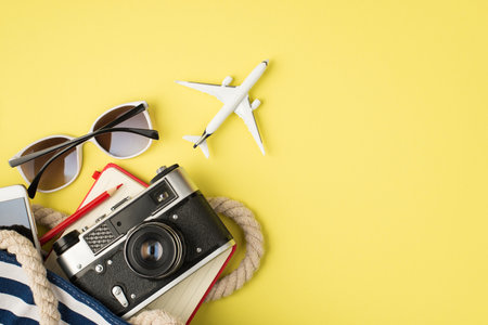 Above photo of sunglasses phone bag camera notebook pencil and plane isolated on the yellow background with blank spaceの写真素材