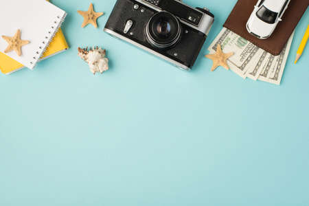 Top view photo of yellow notebooks camera pencil car model on passport cover with dollars seashell and starfishes on isolated pastel blue background with copyspaceの写真素材