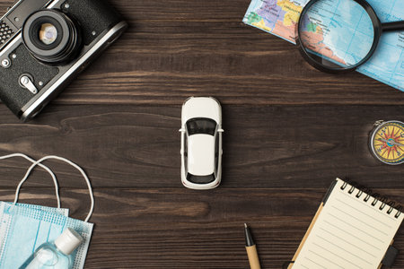 Top view photo of car model in the center camera map magnifier compass notebook pen medical masks and sanitizer on isolated wooden table backgroundの写真素材