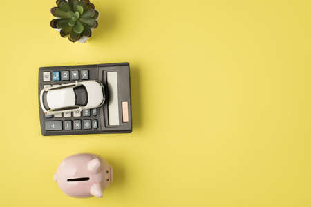 Top view photo of flowerpot car model on calculator and piggy bank on isolated pastel yellow background with copyspaceの写真素材