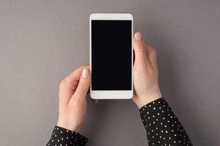 First person top view photo of woman's hands holding smartphone on isolated gray background with...