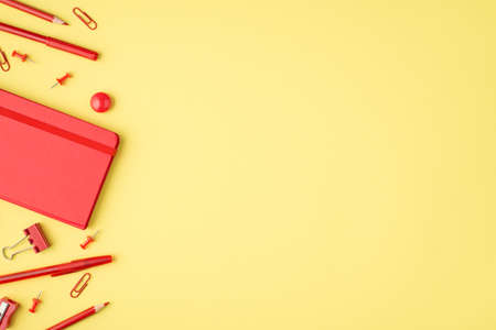 Overhead photo of red notebook watercolor marker pen pencil sharpener and paperclips isolated on the yellow background with copyspaceの写真素材