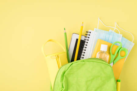 Overhead photo of backpack mask sanitizer notepad pen pencil tablet and pencil-case isolated on the yellow backgroundの写真素材