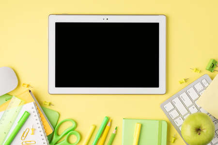 Overhead photo of tablet notebook pen pencil felt-tip scissors ruler paperclips apple computer mouse and keyboard isolated on the yellow backgroundの写真素材