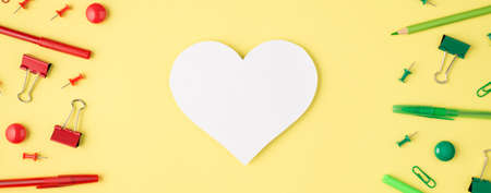 Overhead photo of card paper as heart monochrome green and red stationery pencil pen paperclips and felt-tip isolated on the yellow backgroundの写真素材