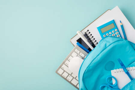 Top view photo of knapsack with tablet computer calculator copybooks pencil pens keyboard mouse and scissors on isolated pastel blue background with copyspaceの写真素材