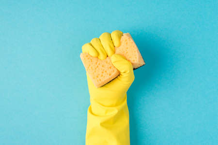 Top view photo of raised hand in yellow rubber glove clenching yellow scouring pad on isolated pastel blue background with copyspaceの写真素材
