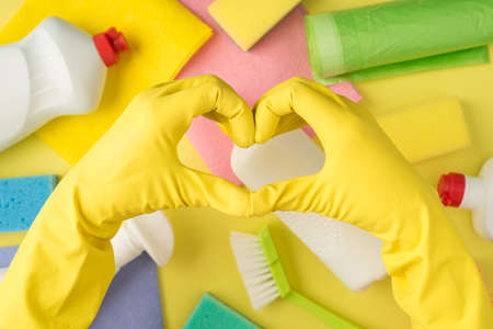 Above pov photo of equipment for cleaning and hands in yellow gloves with gesture as heart isolated on the yellow backgroundの写真素材