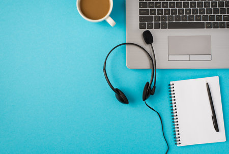 Top view photo of laptop headset with microphone cup of drink and pen on open reminder on isolated pastel blue background with blank spaceの写真素材