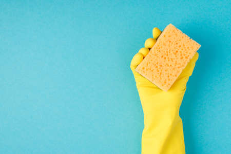 Top view photo of hand in yellow rubber glove holding yellow sponge on isolated pastel blue background with copyspaceの写真素材