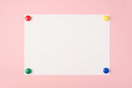 Top view photo of paper sheet with four multicolor magnets in the corners on isolated pastel pink...
