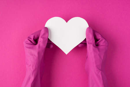 Top view photo of hands in pink gloves holding white paper heart on isolated pink background with blank spaceの写真素材