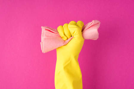Photo of raised hand in yellow glove clenching pastel pink rag into fist on isolated pink background with copyspaceの写真素材