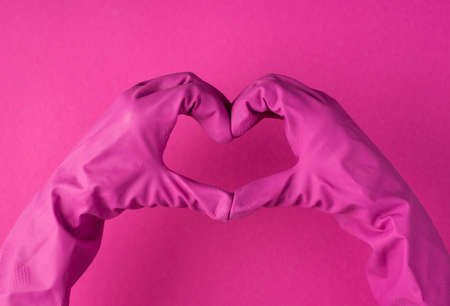Top view photo of hands in pink gloves making heart with fingers on isolated pink background with copyspaceの写真素材