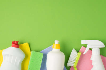 Top view photo of white foam and spray detergent bottles brush scouring pad and multicolor viscose napkins on isolated green background with blank spaceの写真素材
