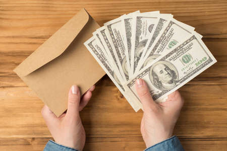 First person top view photo of hands holding fan of hundred dollars banknotes money and craft paper...