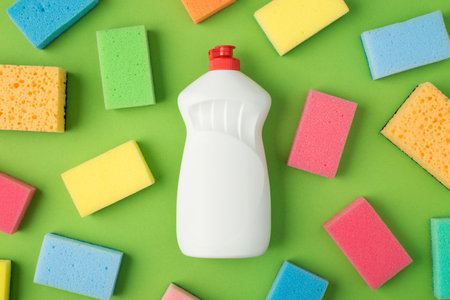 Top view photo of white gel detergent bottle with red cap without label and multicolor scouring pads on isolated green background with copyspaceの写真素材
