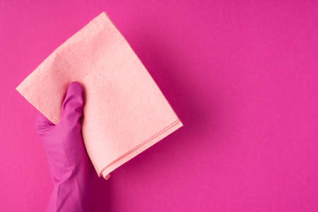 Top view photo of hand in pink glove holding pastel pink napkin on isolated pink background with...