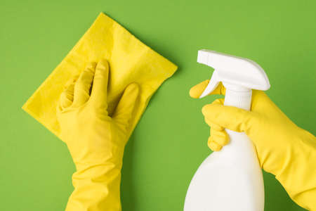Above photo of hands in yellow gloves holding cleaning spray and cleaning rag isolated on the green backgroundの写真素材