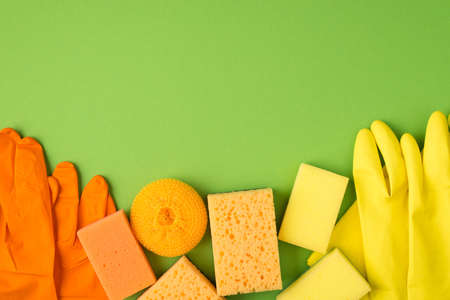 Top view photo of orange and yellow rubber gloves sponges on isolated green background with copyspaceの写真素材