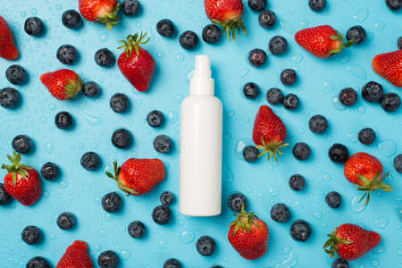 Above photo of strawberries blueberries water drops and white bottle of spray in the middle isolated on the blue backgroundの写真素材