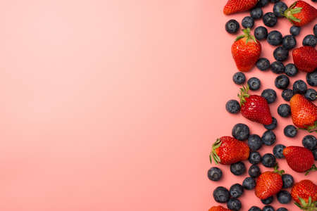 Top view photo of scattered strawberries and blueberries on the right on isolated pastel pink background with copyspace on the leftの写真素材