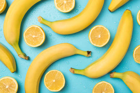 Top view photo of unpeeled yellow bananas cut lemons and water drops on isolated pastel blue backgroundの写真素材