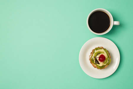 Overhead photo of cup of coffee and plate with fruit cake isolated on the teal backdrop with copyspaceの写真素材