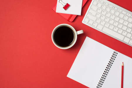 Top view photo of workplace white keyboard red binder clip pencil organizers and cup of coffee on isolated red background with copyspaceの写真素材