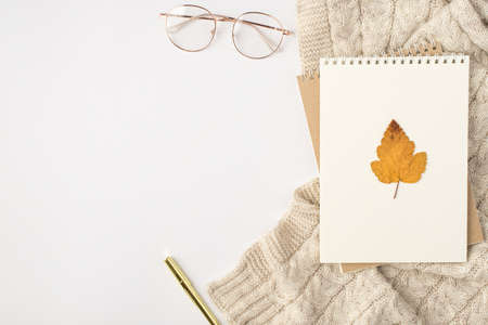 Top view yellow autumn leaf on notepads stylish glasses golden pen and sweaterの写真素材