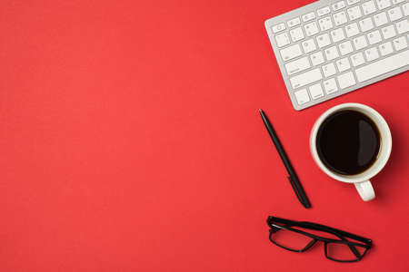 Top view photo of workspace white keyboard pen glasses and cup of coffee on isolated red background with empty spaceの写真素材
