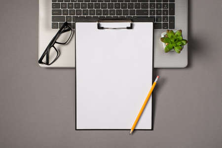 Top view photo of black clipboard folder with white paper sheet pencil glasses and flowerpot on gray...