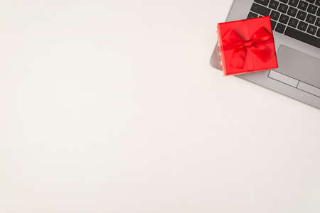 Top view photo of red little giftbox with ribbon bow on laptop on isolated white wooden background with copyspaceの写真素材