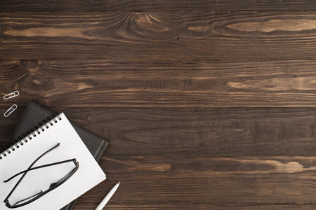 Top view photo of white clips pen and glasses on two black and white notebooks on isolated dark wooden table background with copyspaceの写真素材