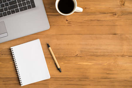 Top view photo of laptop cup of coffee pen and spiral planner on isolated wooden table background...