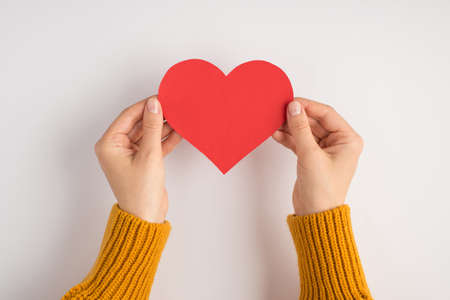 First person photo of woman's hands in yellow pullover holding red paper heart on isolated white background with blank spaceの写真素材