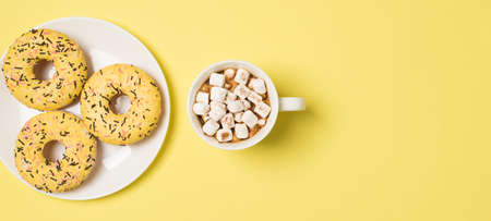 Top view photo of cup of drink with marshmallow and plate with three yellow glazed donuts on isolated pastel yellow background with copyspaceの写真素材