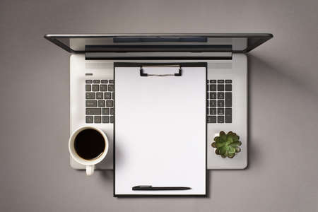 Top view photo of black clipboard with white sheet of paper pen cup of drink and plant on open...
