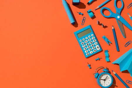 Top view photo of blue school accessories stationery calculator markers pencils clips pushpins scissors paper airplane and alarm clock on isolated orange background with copyspaceの写真素材