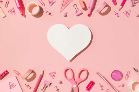 Overhead photo of scissors tape paper clips triangle pins spirals pencil pen eraser marker and white paper heart isolated on the pink backdropの写真素材