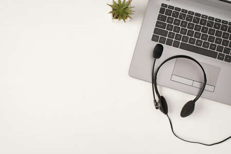 Top view photo of black wired headset on gray laptop and plant on isolated white wooden table background with empty spaceの写真素材