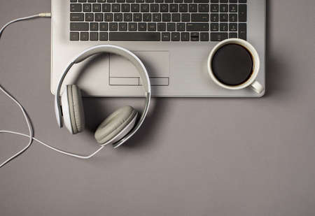 Top view photo of wired white headphones and cup of coffee on laptop keyboard on isolated gray backgroundの写真素材