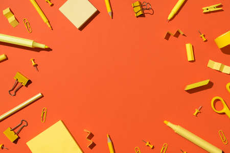 Top view photo of yellow stationery school supplies scissors pencils markers binder clips pushpins and sticky note paper on isolated vivid orange background with copyspace in the middleの写真素材