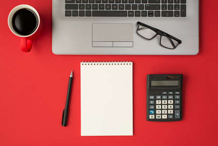 Top view photo of glasses on laptop red cup of coffee pen calculator and notebook on isolated red background with copyspaceの写真素材