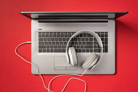 Overhead photo of gray laptop and headphones isolated on the red backdropの写真素材