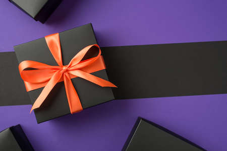 Top view photo of black giftbox with orange ribbon bow boxes on isolated violet and black background...