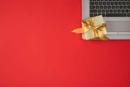 Top view photo of small golden giftbox with ribbon bow on laptop on isolated red background with empty spaceの写真素材