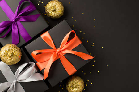 Top view photo of three black gift boxes with violet orange and white ribbon bows golden confetti and shiny golden pumpkins on isolated black background with blank spaceの写真素材